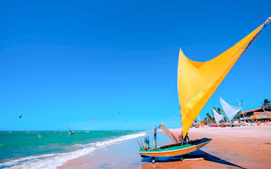 Traditional jangada boat on Cumbuco beach with kitesurfers in the ocean, Sao Paulo tour.