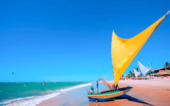 Traditional jangada boat on Cumbuco beach with kitesurfers in the ocean, Sao Paulo tour.