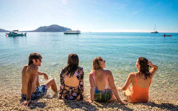 Tourists sitting on Fitzroy Island beach with boats in the background.