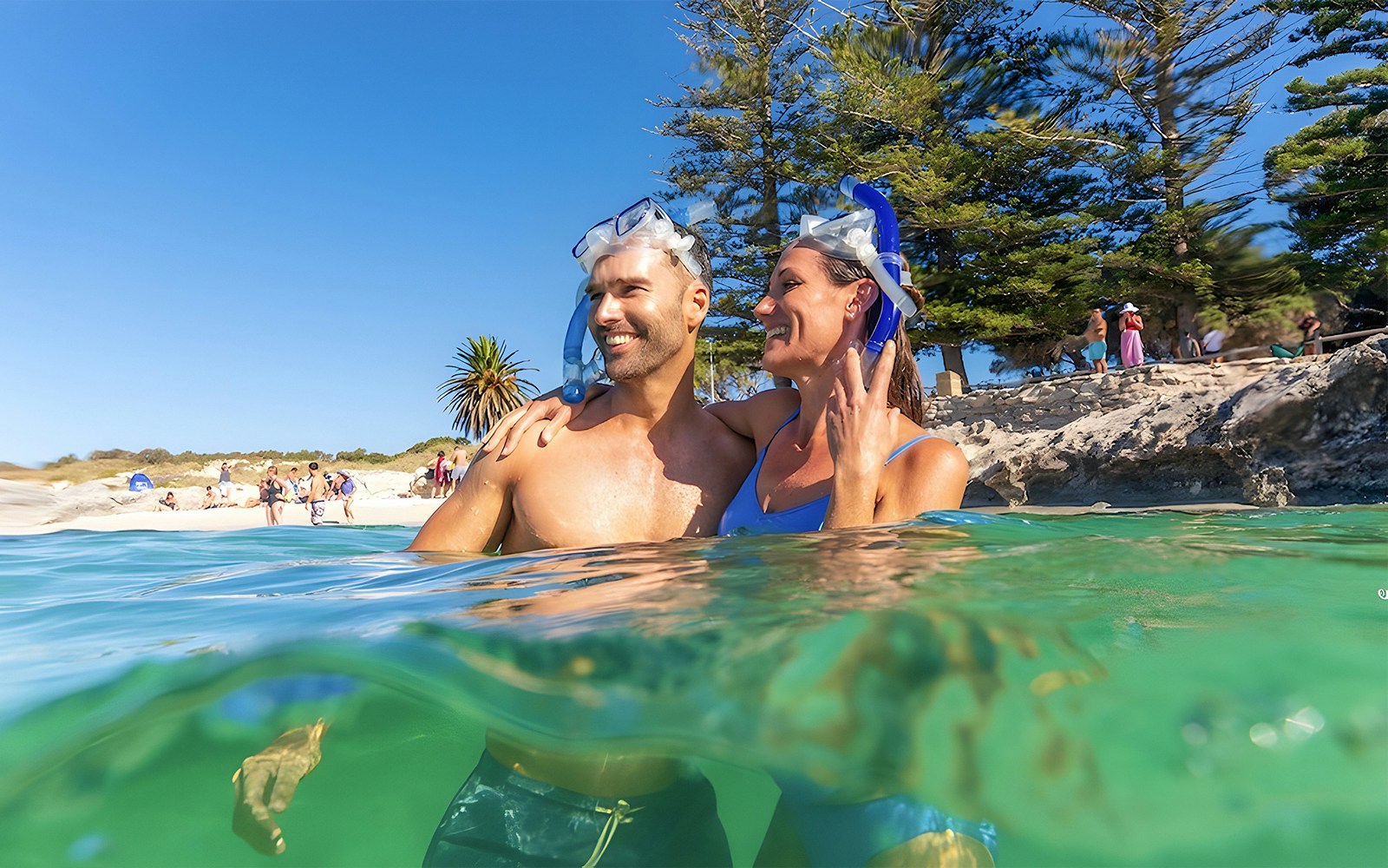 Couple snorkeling near Rottnest Island beach with clear water and trees in the background.