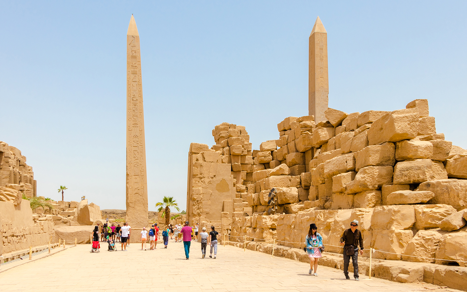 Visitors walking through Luxor Temple with ancient obelisks and stone ruins in Egypt.