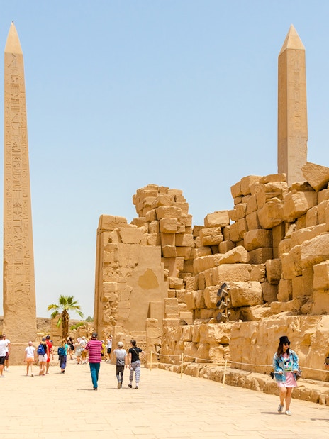 Visitors walking through Luxor Temple with ancient obelisks and stone ruins in Egypt.
