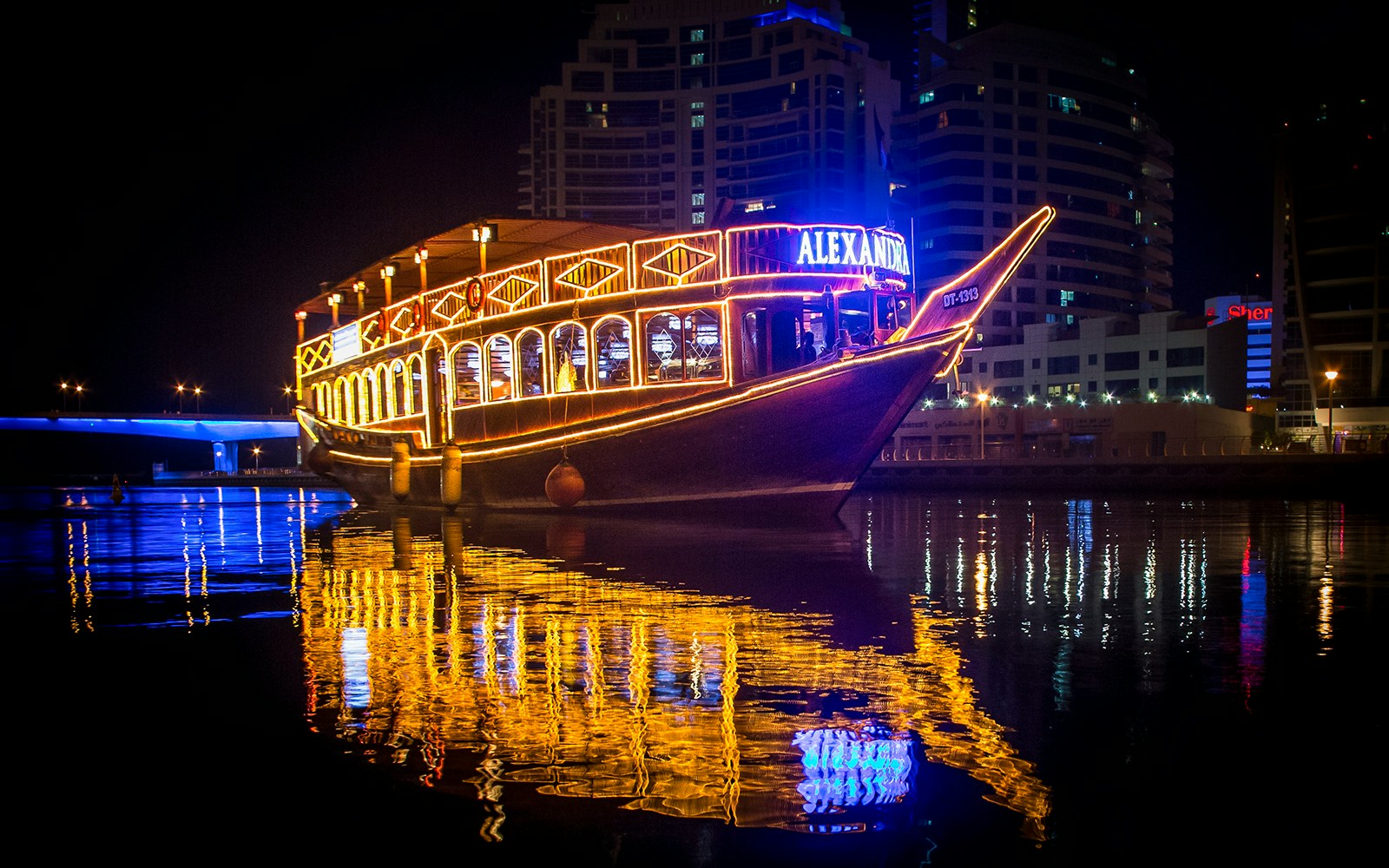 Alexandra Dhow Cruise lit up at night in Dubai Marina, reflecting on the water.