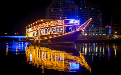 Alexandra Dhow Cruise lit up at night in Dubai Marina, reflecting on the water.
