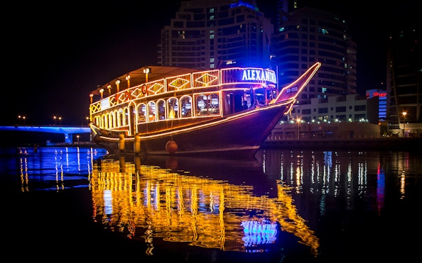 Alexandra Dhow Cruise lit up at night in Dubai Marina, reflecting on the water.