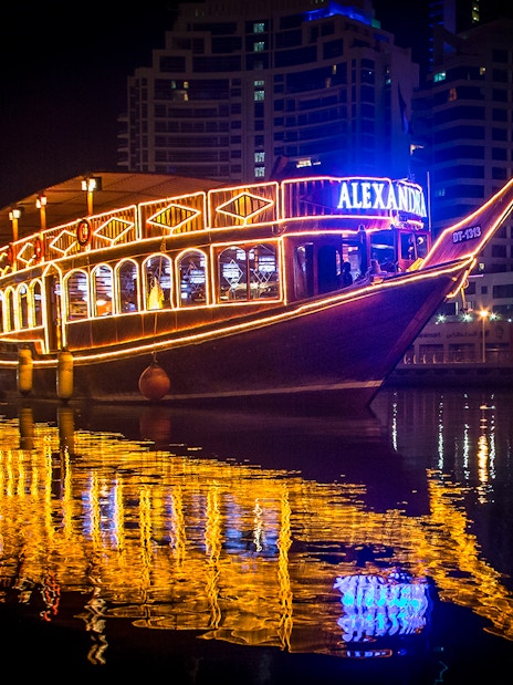 Alexandra Dhow Cruise lit up at night in Dubai Marina, reflecting on the water.