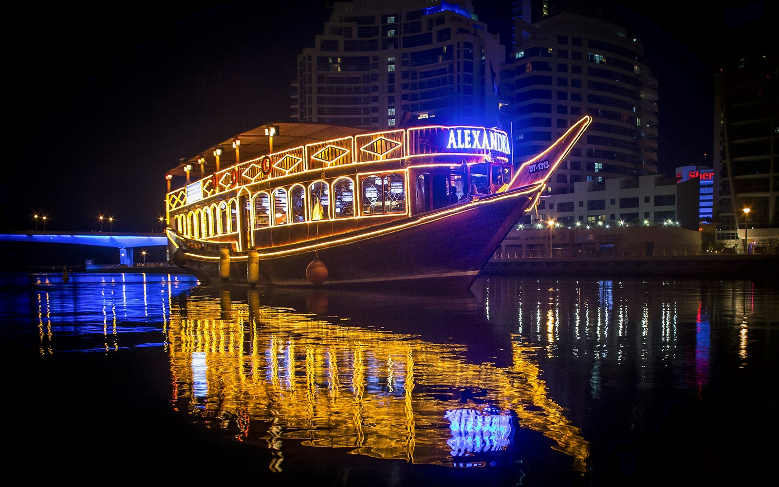 Alexandra Dhow Cruise lit up at night in Dubai Marina, reflecting on the water.