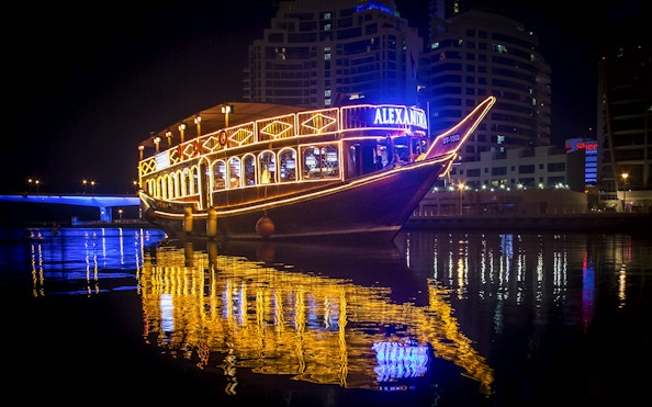 Alexandra Dhow Cruise lit up at night in Dubai Marina, reflecting on the water.