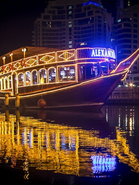 Alexandra Dhow Cruise lit up at night in Dubai Marina, reflecting on the water.