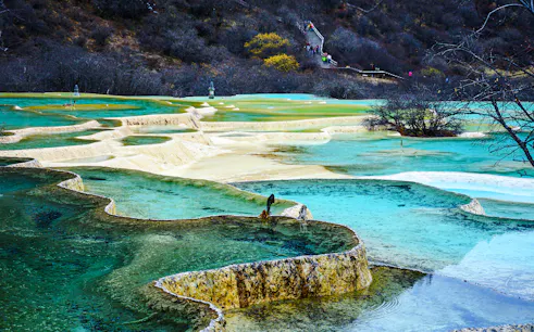 Huanglong National Park's colorful terraced pools, Chengdu, with distant visitors on a walkway.
