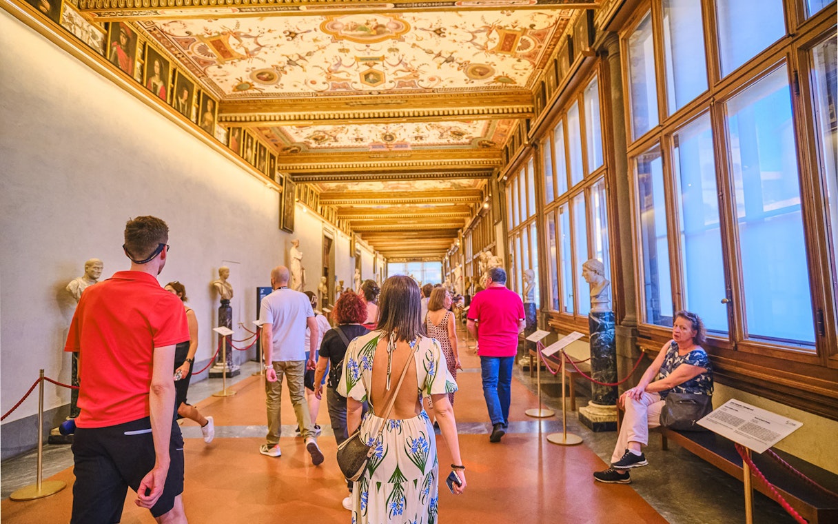 Visitors walking through the Vasari Corridor with sculptures and paintings, Florence.
