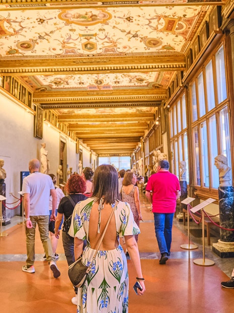 Visitors walking through the Vasari Corridor with sculptures and paintings, Florence.