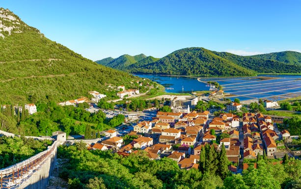 Panoramic view of Ston with historic walls, red-roofed buildings, and surrounding green hills.