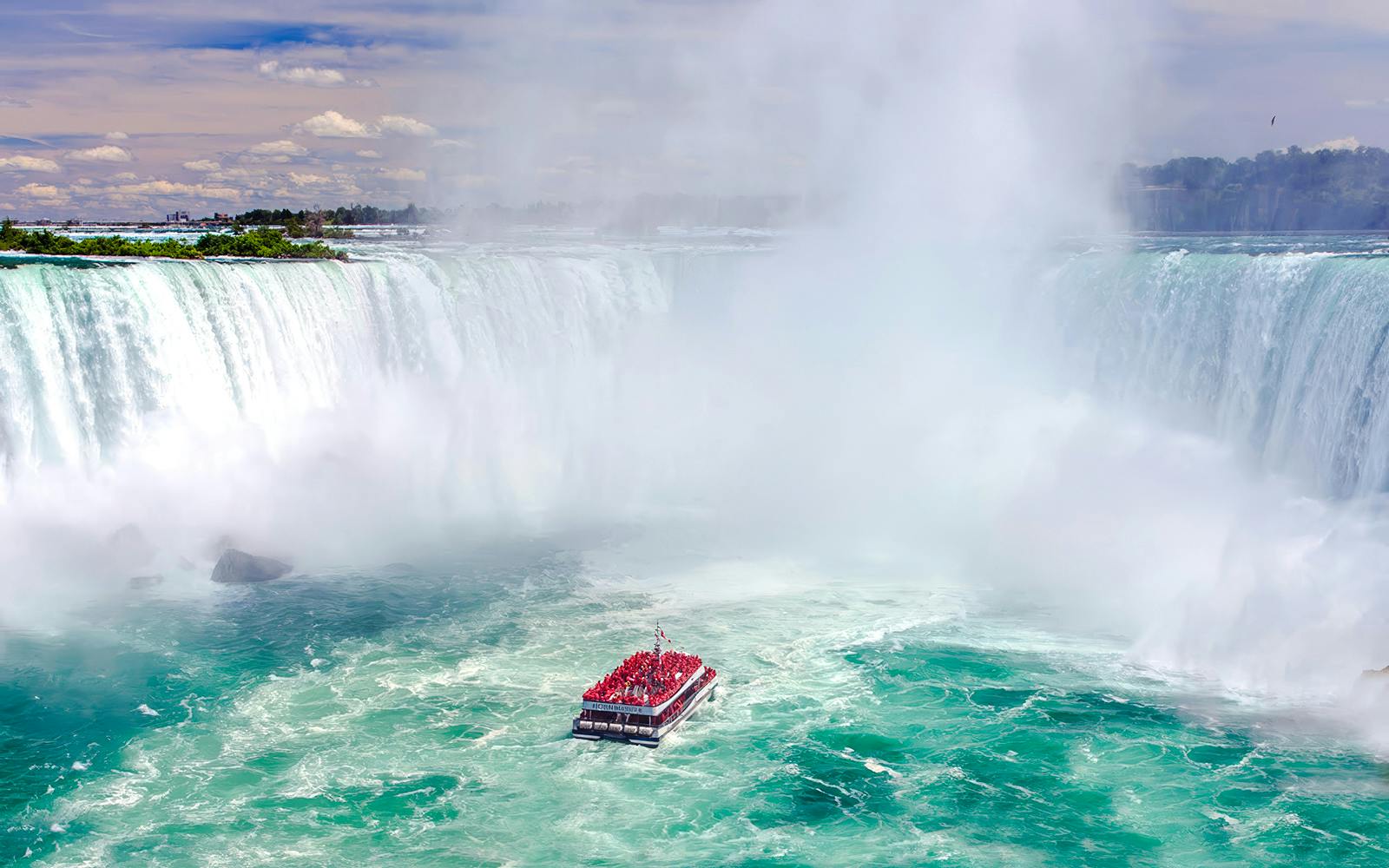 Boat tour approaching Niagara Falls, Canada with mist rising from the waterfall.