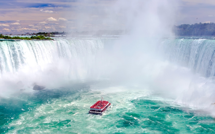 Boat tour approaching Niagara Falls, Canada with mist rising from the waterfall.
