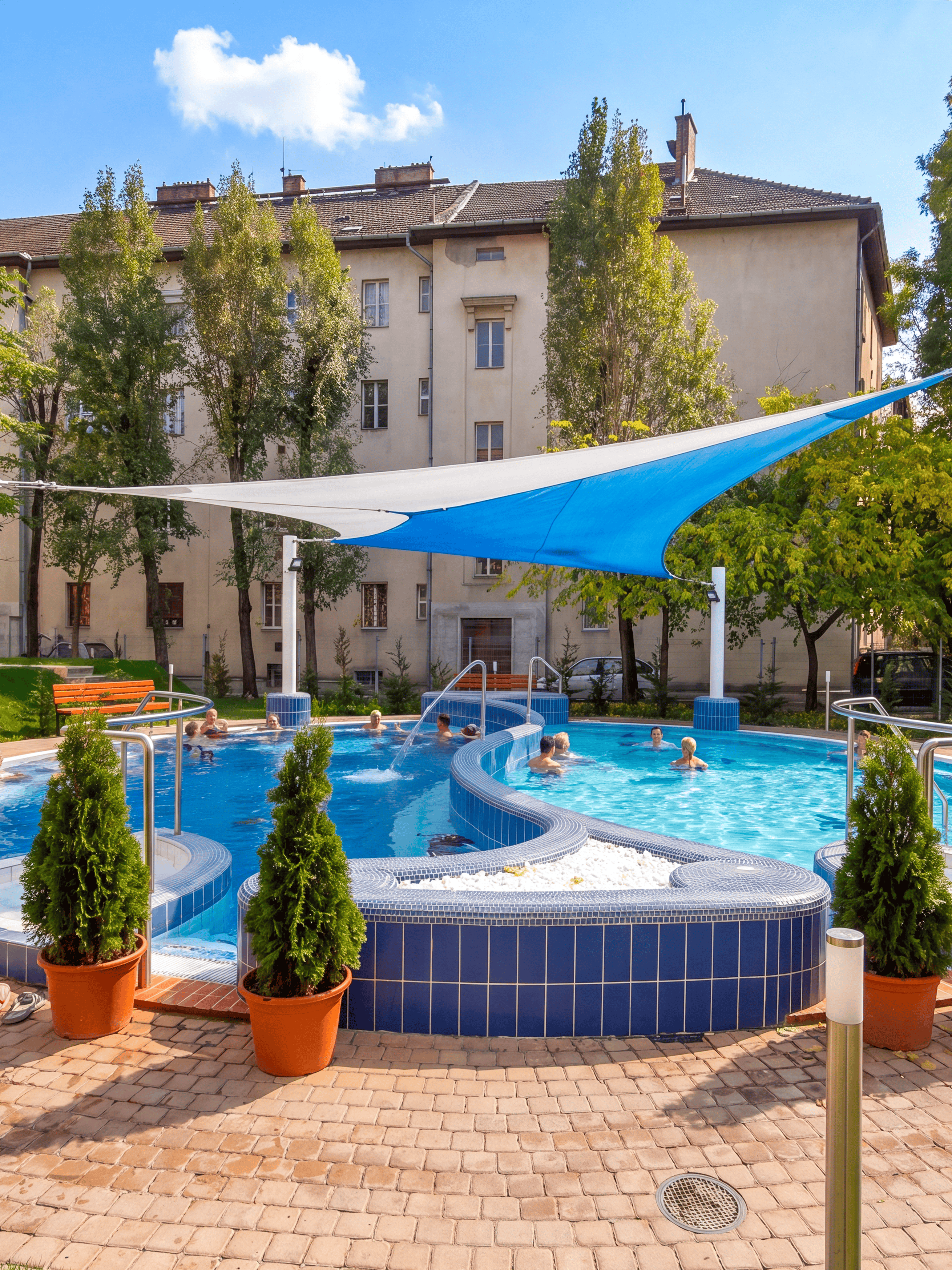 Outdoor pool area at Dandar Spa with people relaxing in the water, surrounded by trees and buildings.