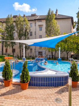 Outdoor pool area at Dandar Spa with people relaxing in the water, surrounded by trees and buildings.
