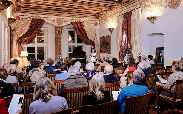 Audience attending a Chopin piano concert in an ornate room with a grand piano.