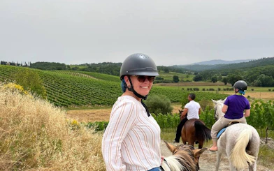 Horseback riders in Chianti countryside vineyard during Tuscany winery tour.