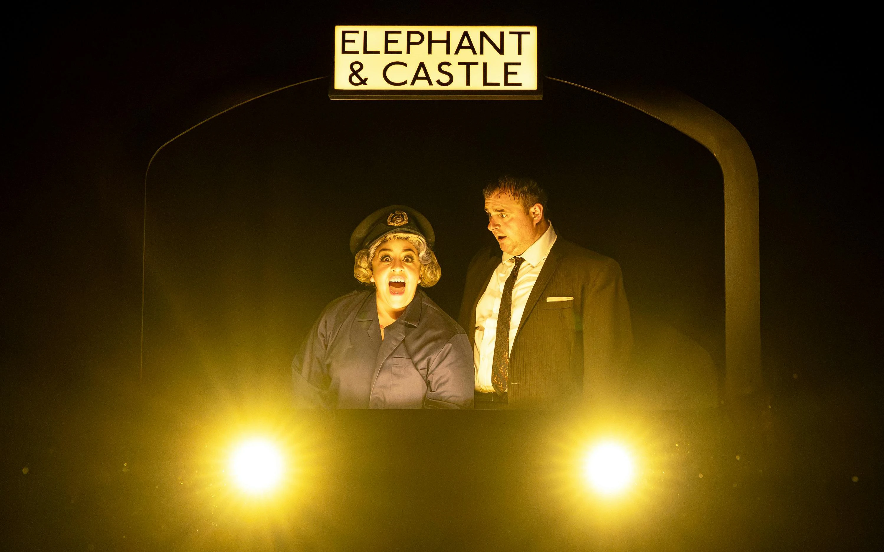 Actors performing "The Comedy About Spies" under Elephant & Castle sign.
