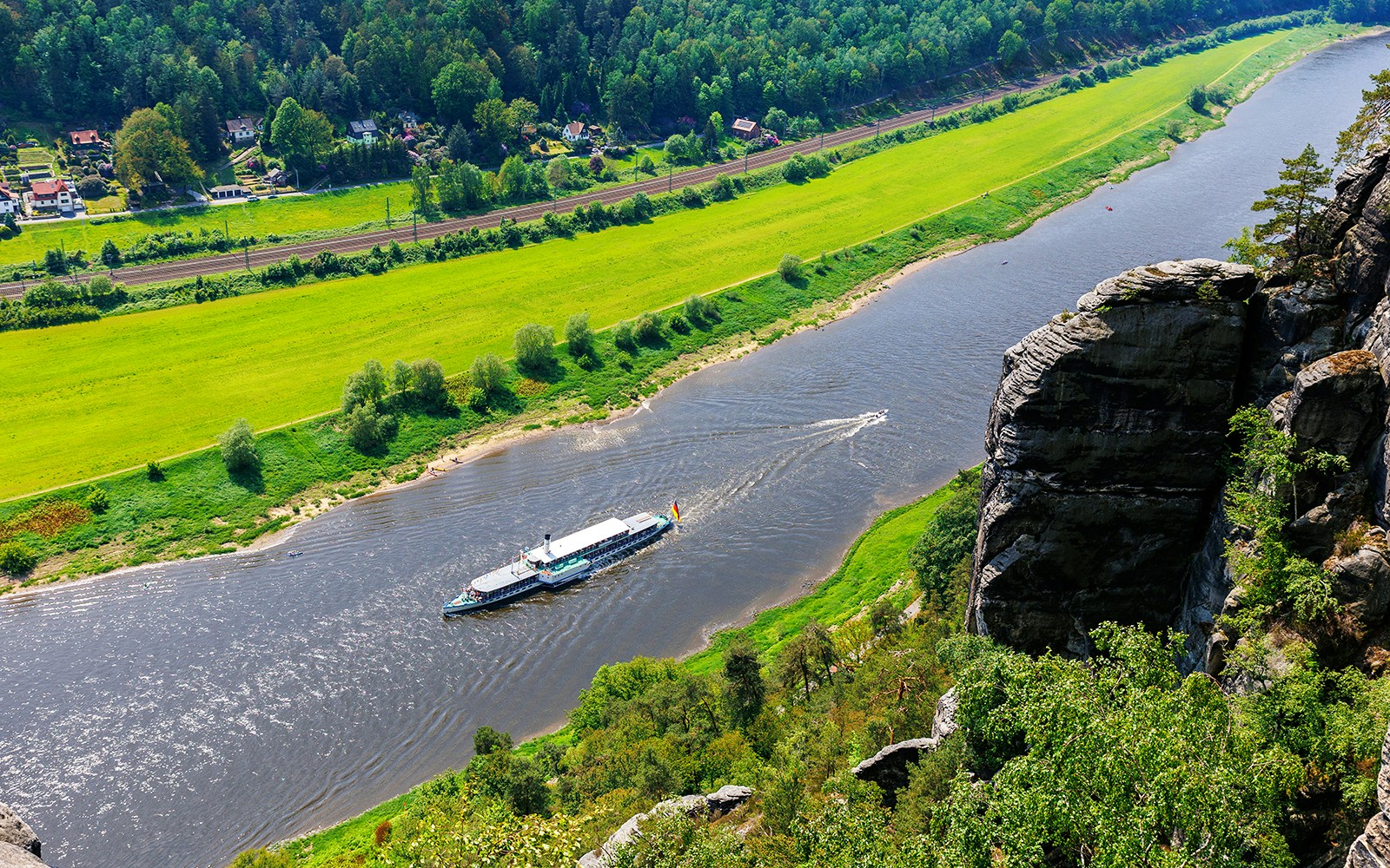 Paddle-steamer cruising on the Elbe River in Saxony, surrounded by lush greenery and rocky cliffs.