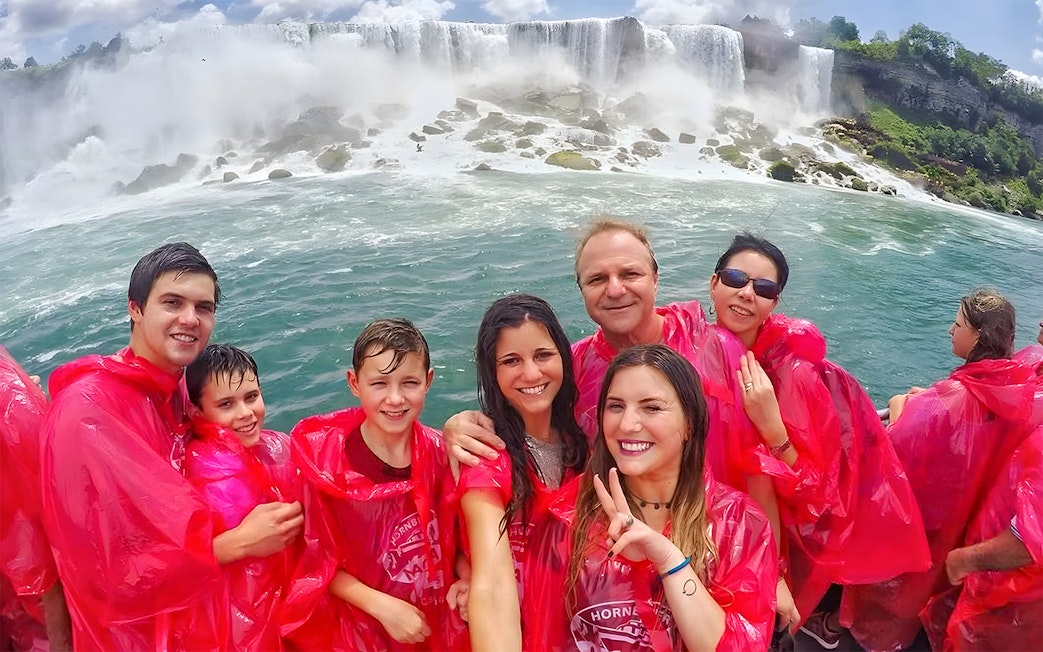 Tourists in red ponchos on a Niagara Falls cruise with waterfalls in the background.