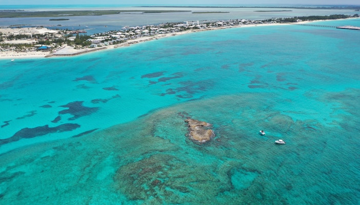 Aerial view of boats near coral rocks with North Bimini coast in background.