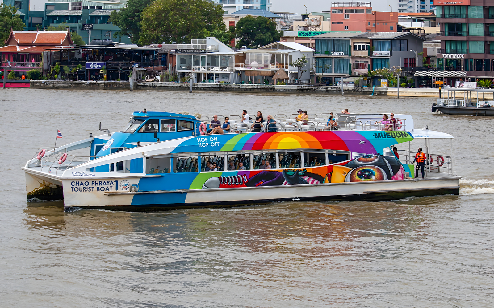 Chao Phraya tourist boat on Bangkok river with colorful design and passengers on deck.