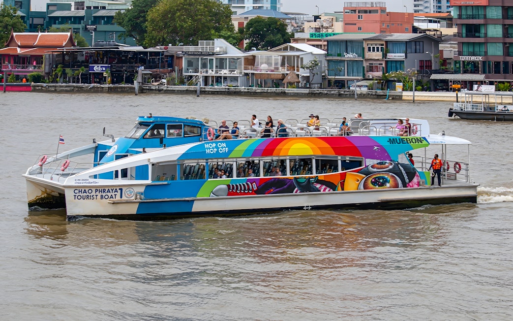 Chao Phraya tourist boat on Bangkok river with colorful design and passengers on deck.