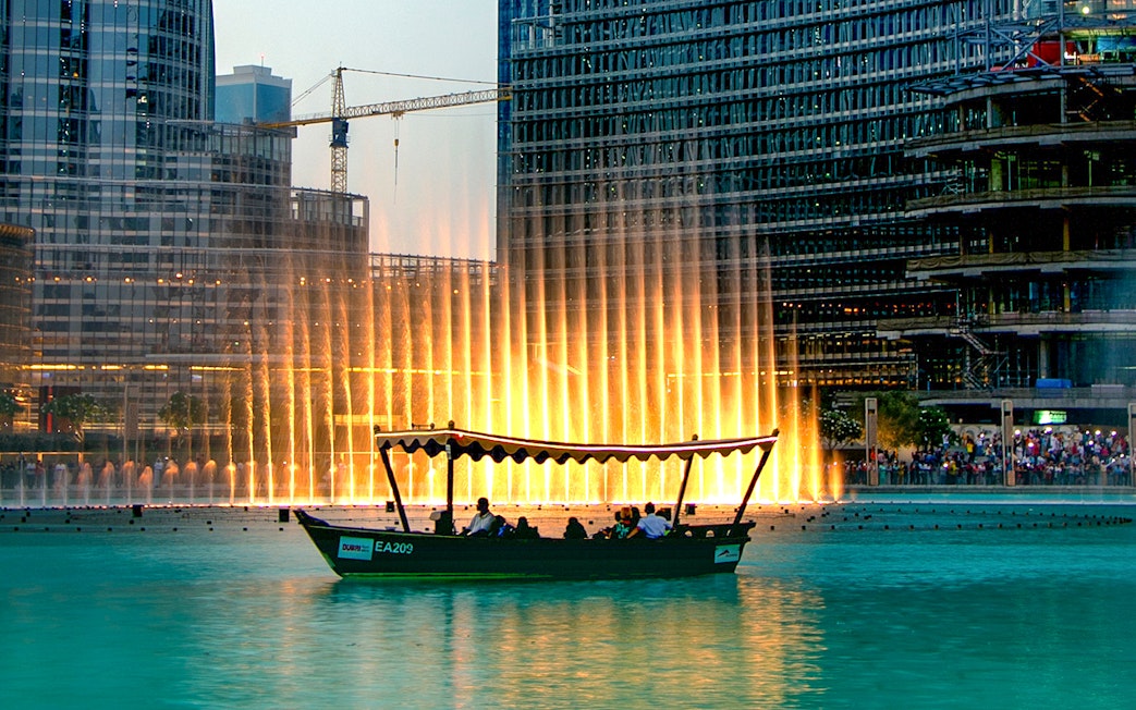 Traditional abra boat on Dubai Lake with fountain show in the background.