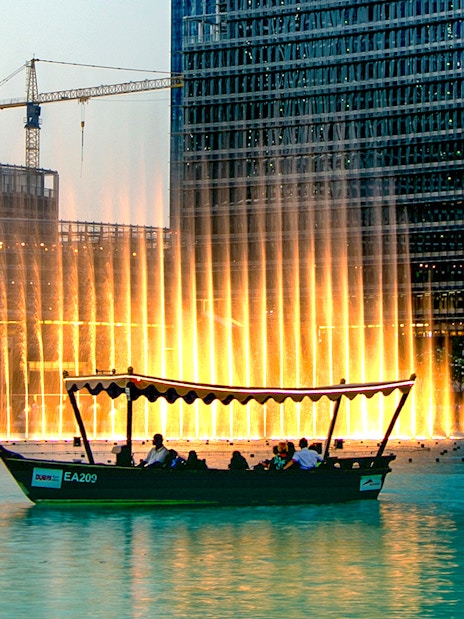 Traditional abra boat on Dubai Lake with fountain show in the background.