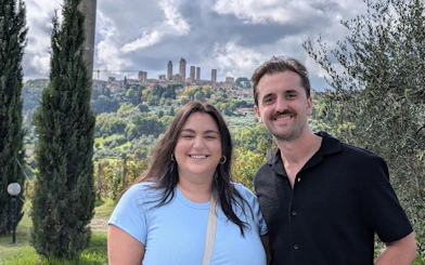Couple smiling with San Gimignano towers in the background during Tuscany wine tour.