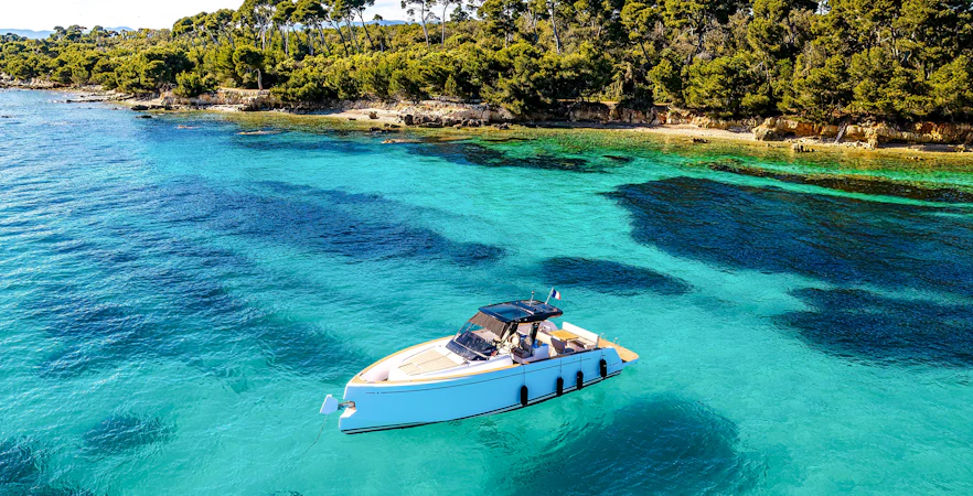 Boat on turquoise waters near Lérins Island with lush green shoreline.