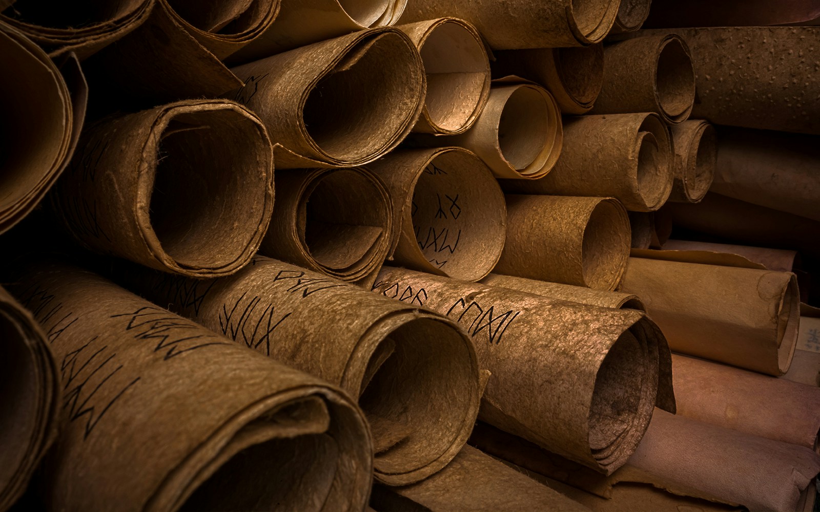 Ancient scrolls with inscriptions stacked in a dimly lit archive.
