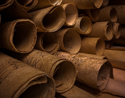 Ancient scrolls with inscriptions stacked in a dimly lit archive.