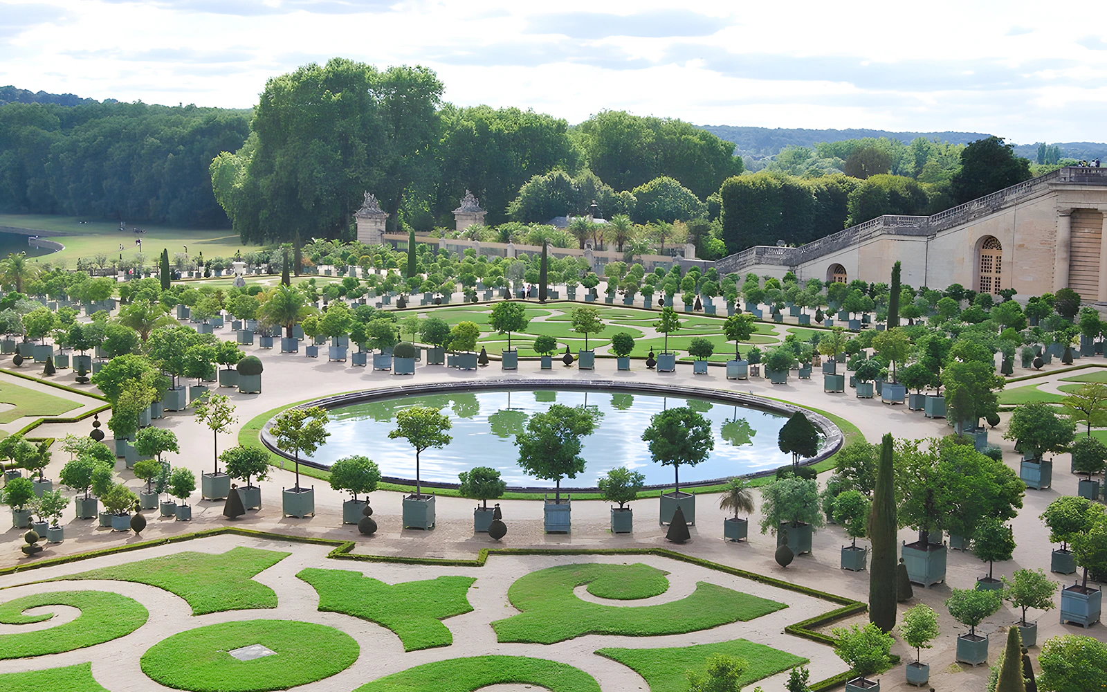 Palace of Versailles gardens with manicured lawns and circular pond.