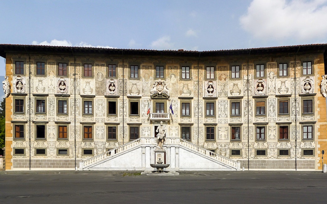 Facade of Palazzo della Carovana in Pisa with ornate sculptures and detailed frescoes.