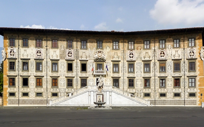 Facade of Palazzo della Carovana in Pisa with ornate sculptures and detailed frescoes.