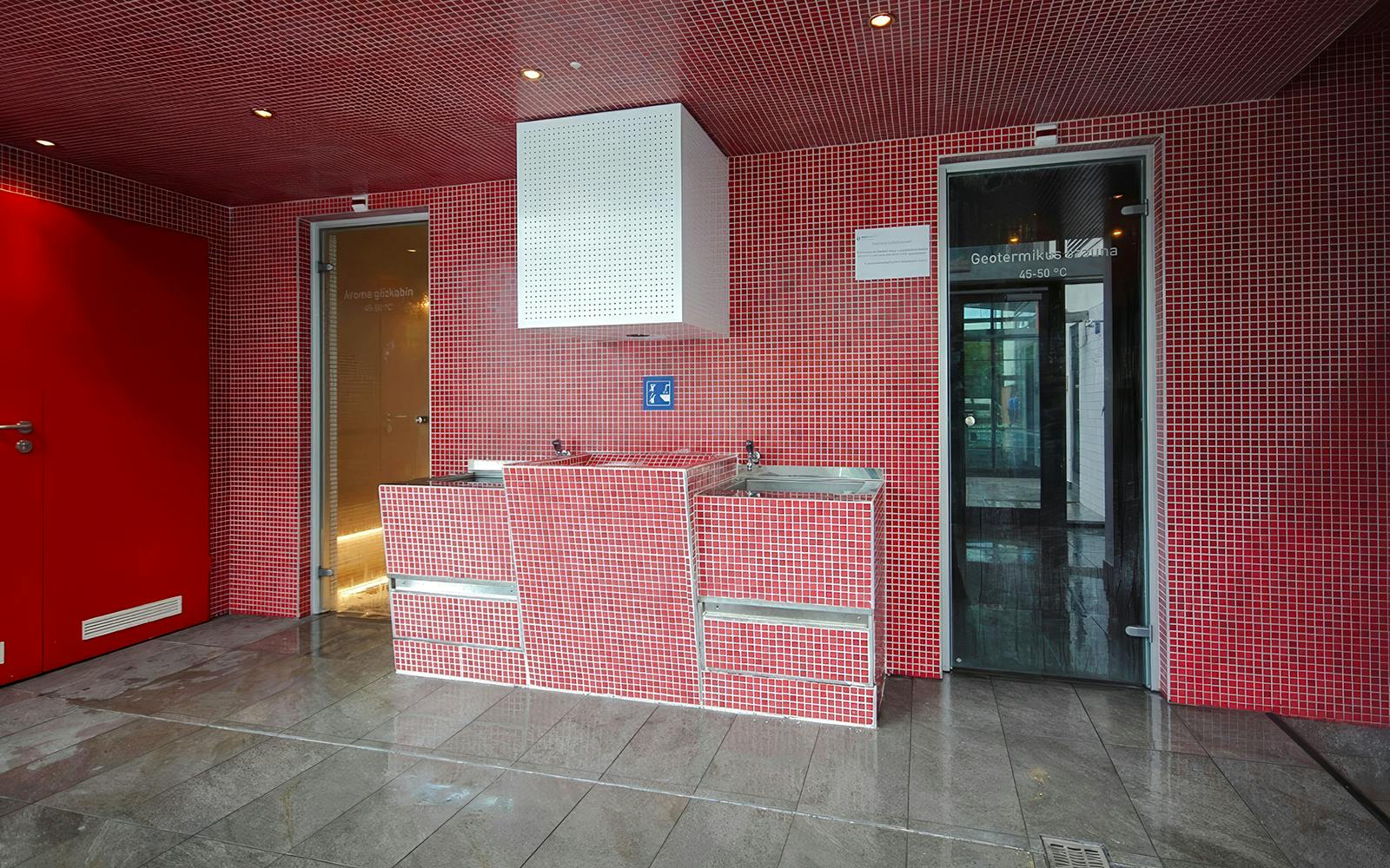 Red-tiled interior of Paskal Thermal Bath in Budapest with sinks and sauna doors.