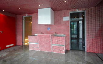 Red-tiled interior of Paskal Thermal Bath in Budapest with sinks and sauna doors.