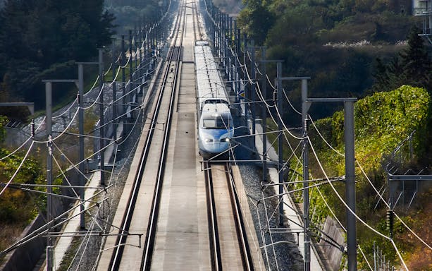 High-speed KTX train on tracks surrounded by greenery in Korea.
