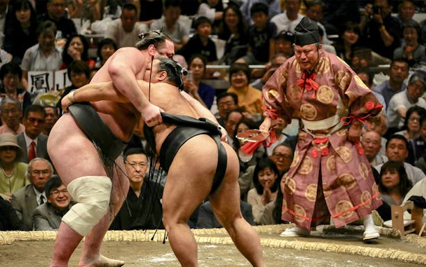 Sumo wrestlers competing at a Sumo Tournament with a referee observing.