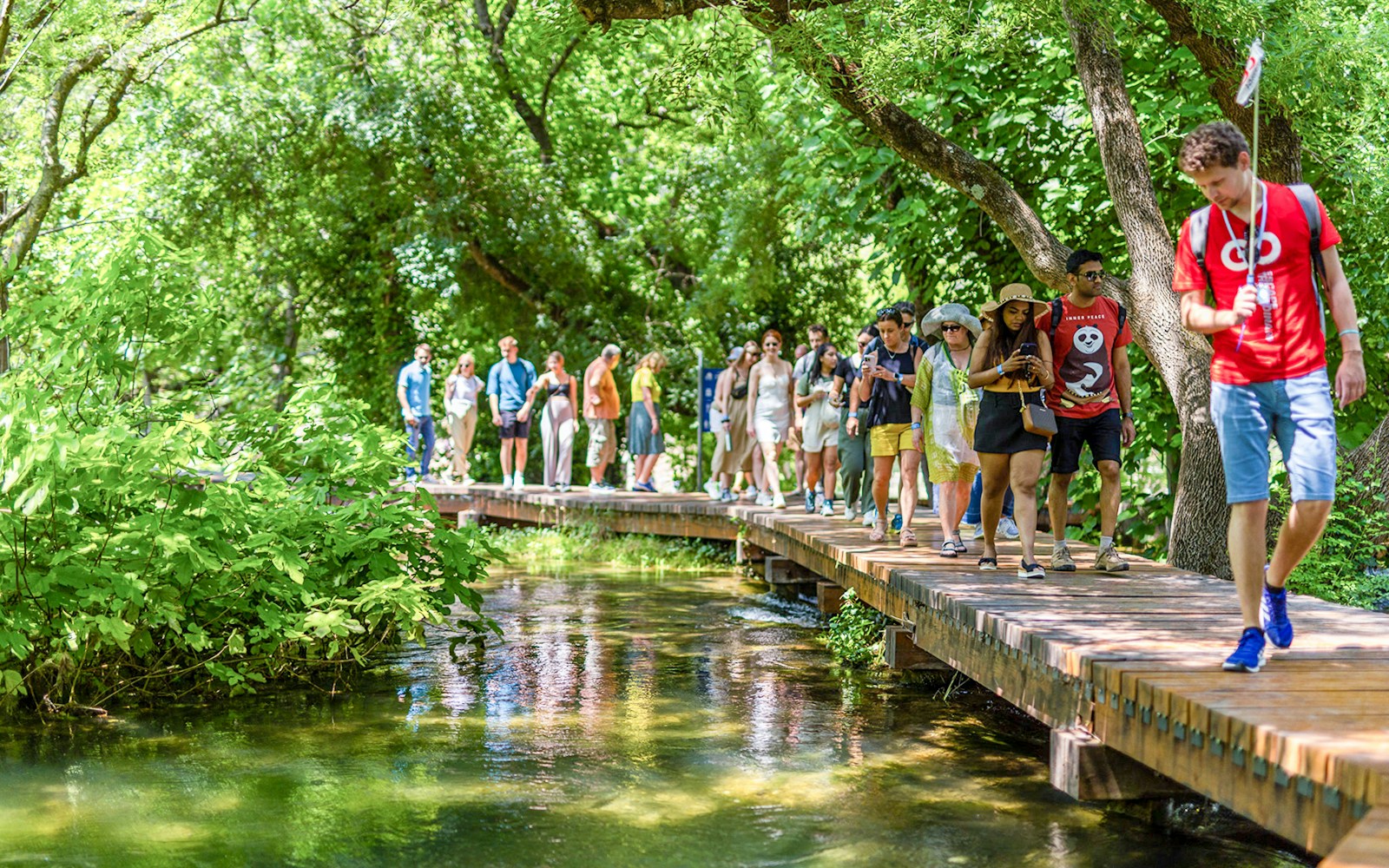 Tourists walking on a wooden path through lush greenery at Krka Waterfalls, Split day trip.