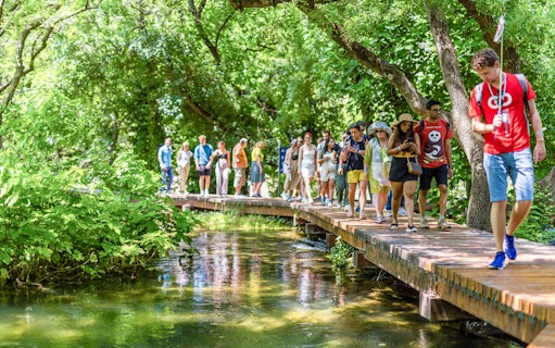 Tourists walking on a wooden path through lush greenery at Krka Waterfalls, Split day trip.