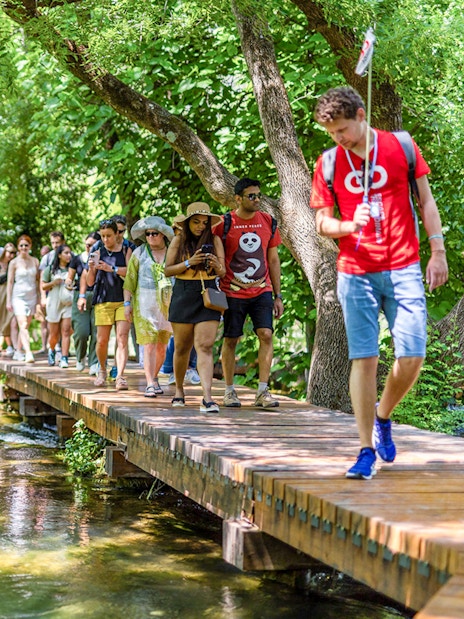 Tourists walking on a wooden path through lush greenery at Krka Waterfalls, Split day trip.