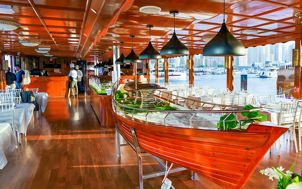 Luxury dhow dinner cruise setup with tables and Dubai Marina view.