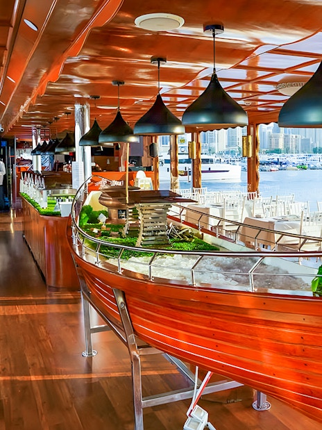 Luxury dhow dinner cruise setup with tables and Dubai Marina view.
