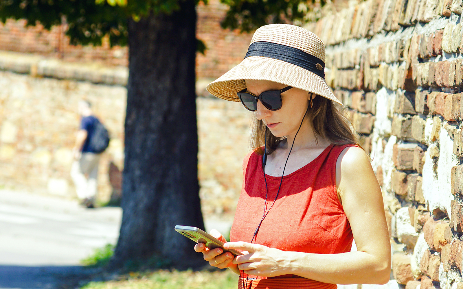 Woman using phone with audio guide near brick wall.