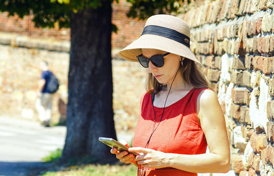 Woman using phone with audio guide near brick wall.