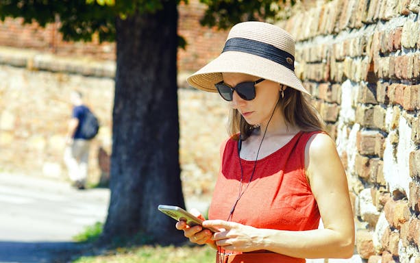 Woman using phone with audio guide near brick wall.